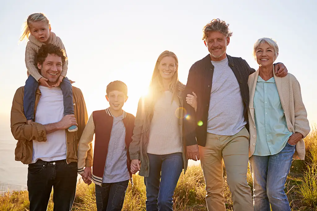 Mehrere Generationen einer Familie gehen Arm in Arm entspannt lächelnd auf die Betrachterin zu